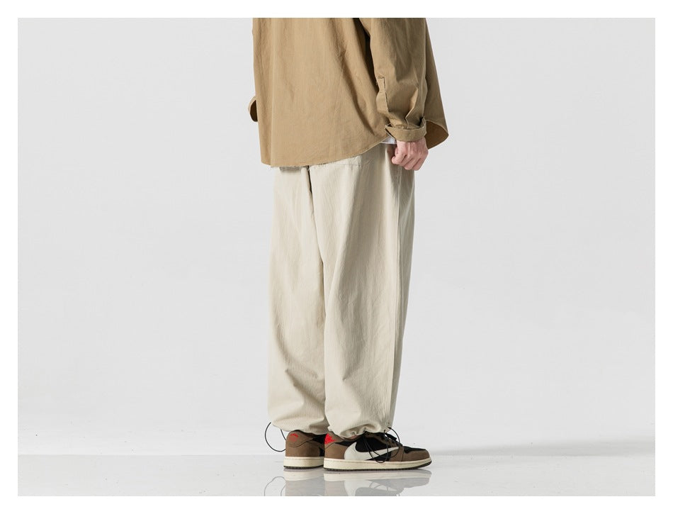 Rear view of a model wearing loose light beige trousers with gathered hems.