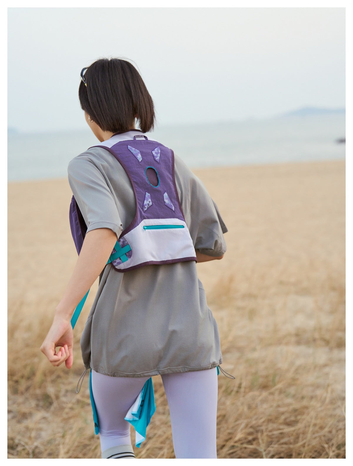 Rear view of a person wearing a purple-and-white running vest with turquoise accents outdoors.