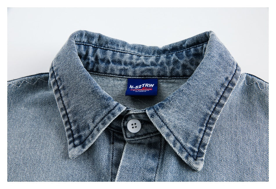 Close-up of the light blue denim shirt collar, top button, stitching, and sewn-in brand label.