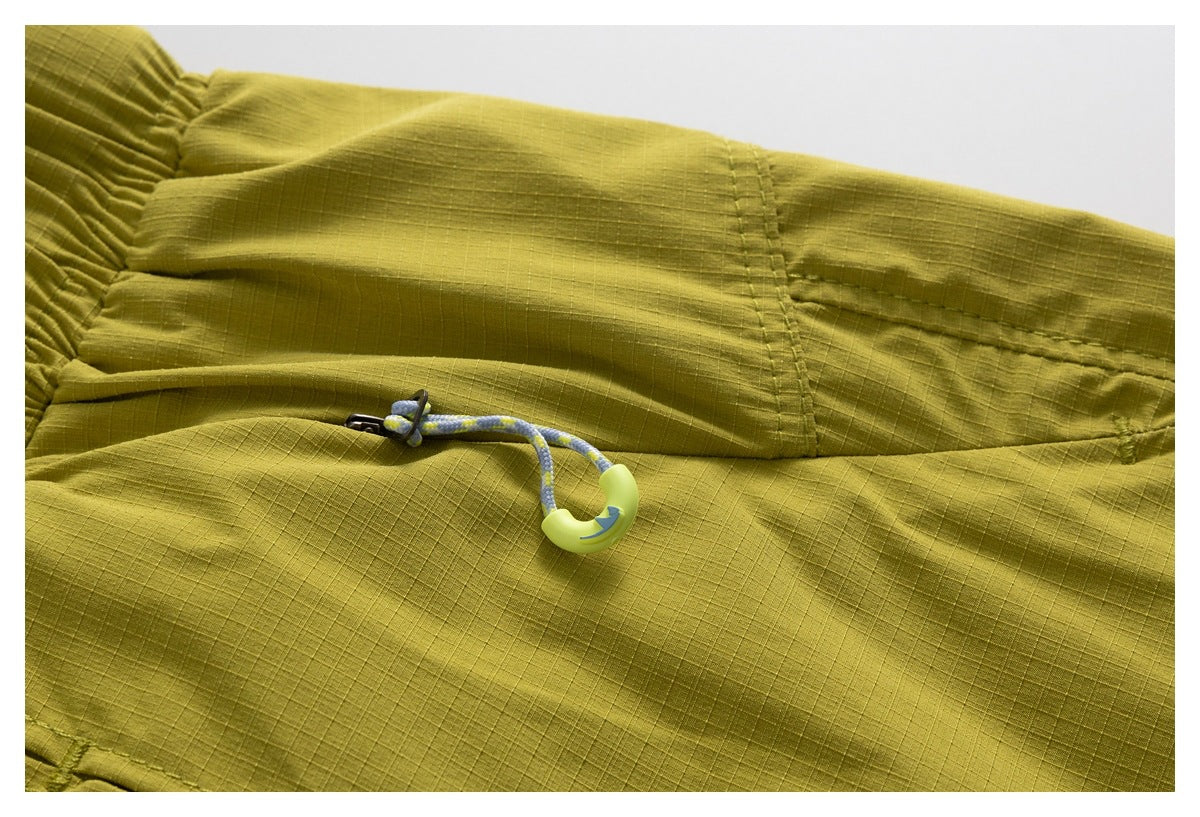Close-up of olive-yellow shorts showing a pocket seam and a blue-and-yellow drawcord toggle.