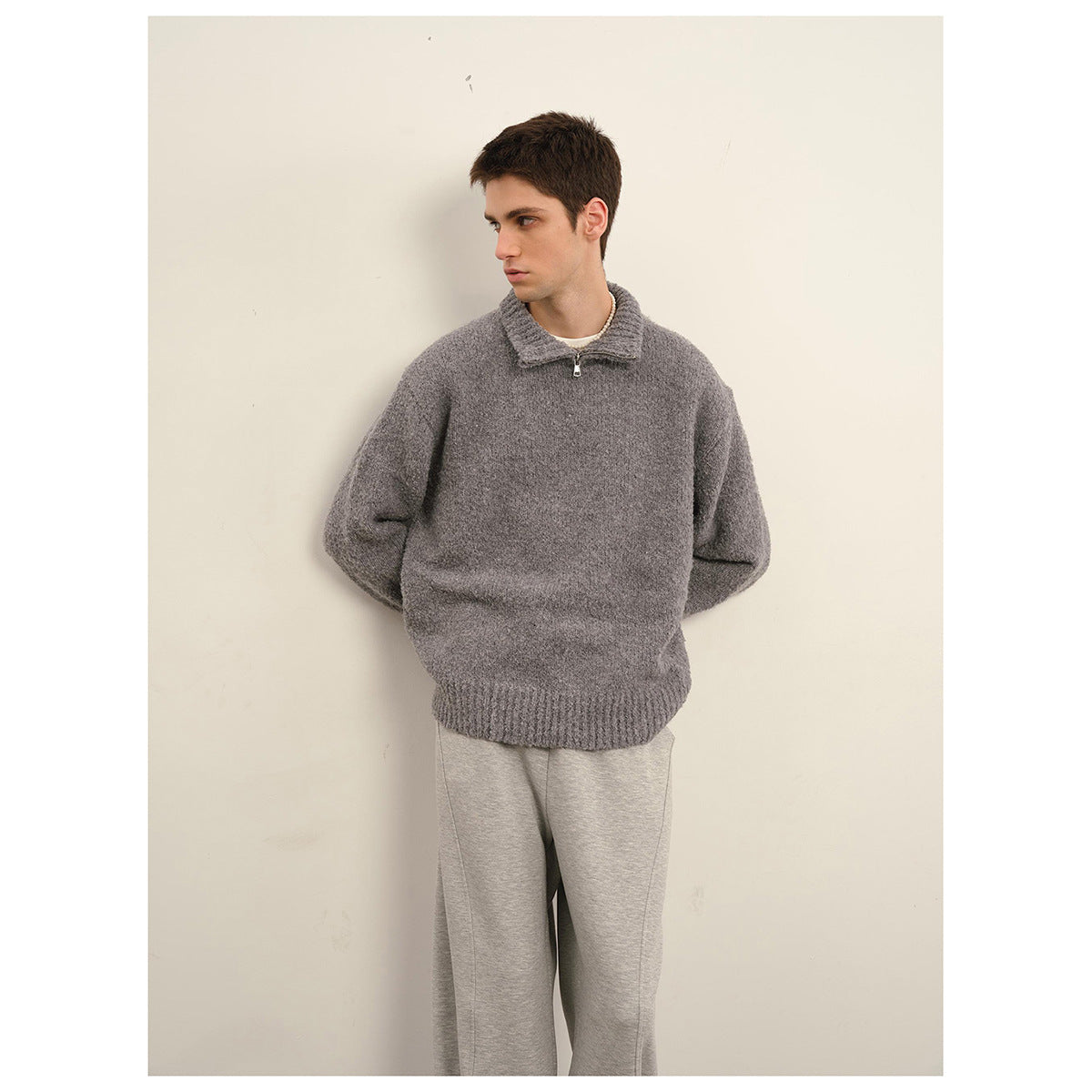 Man wearing a charcoal gray fuzzy knit quarter-zip sweater with a ribbed collar and hem, paired with gray pants.