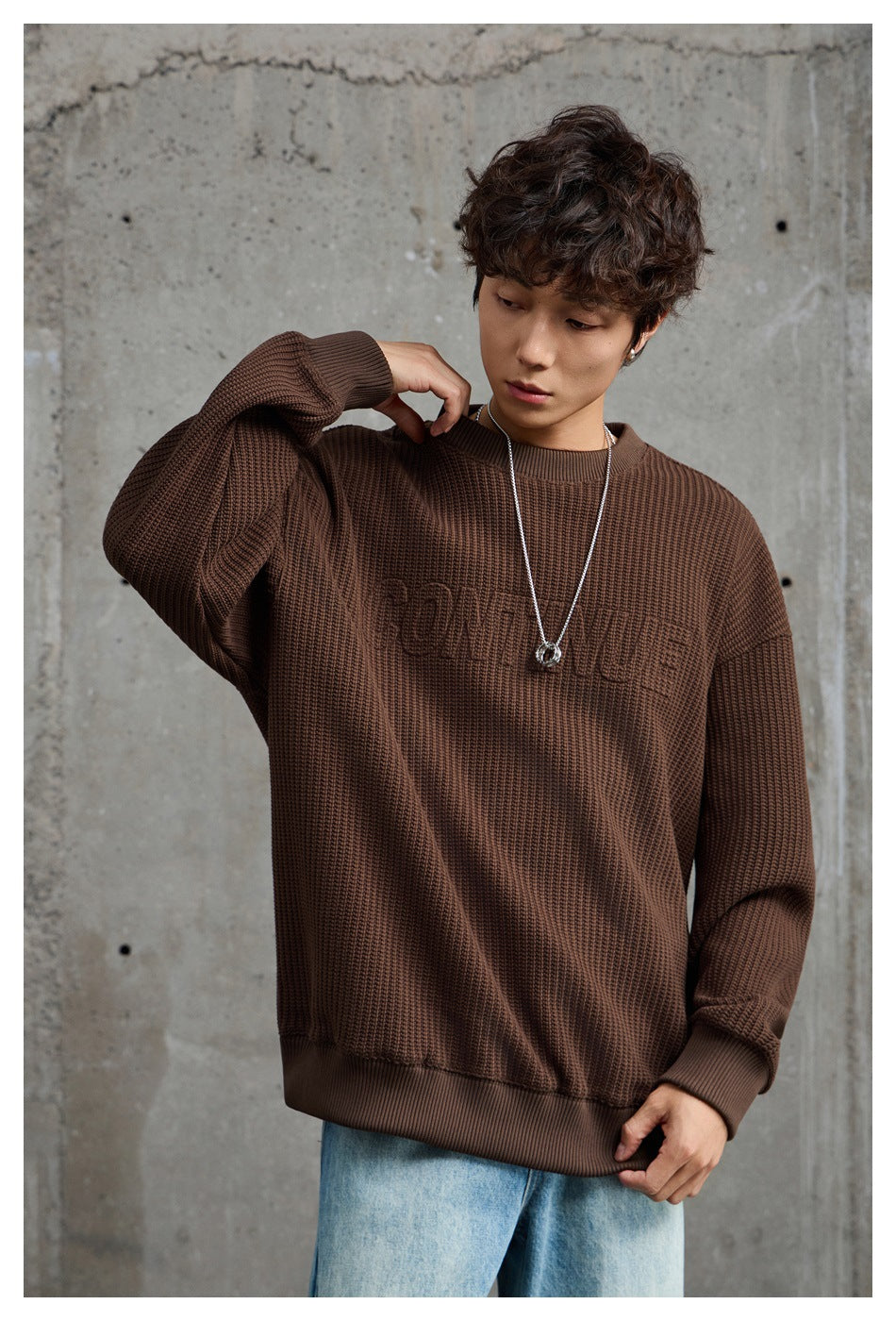 Model wearing a dark brown textured crewneck sweater with ribbed cuffs and hem, paired with light-wash jeans.