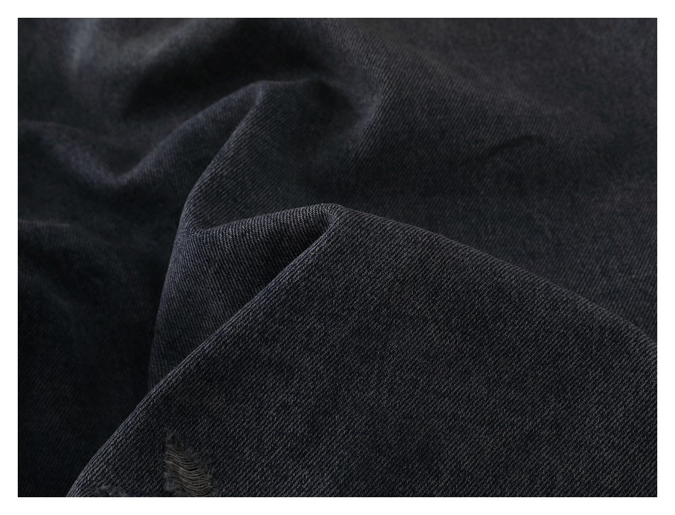 Close-up of dark charcoal denim with a small frayed tear.