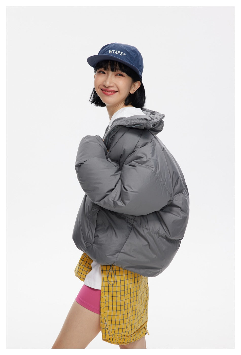 Model in a charcoal-gray puffer jacket, shown from a rear three-quarter angle with the hood down.