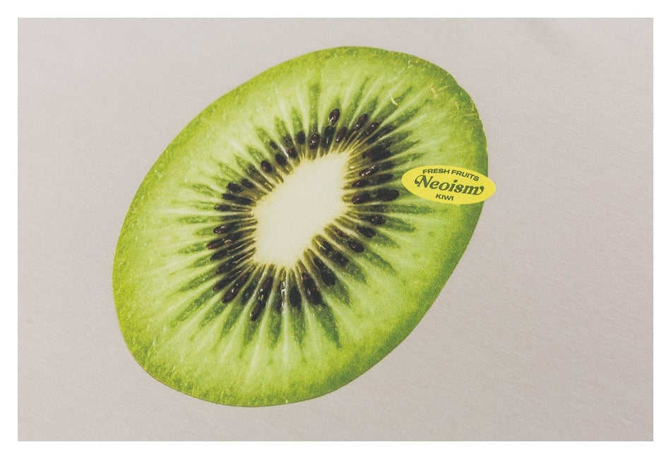 Close-up of a large green kiwi slice graphic with small English print on beige T-shirt fabric.