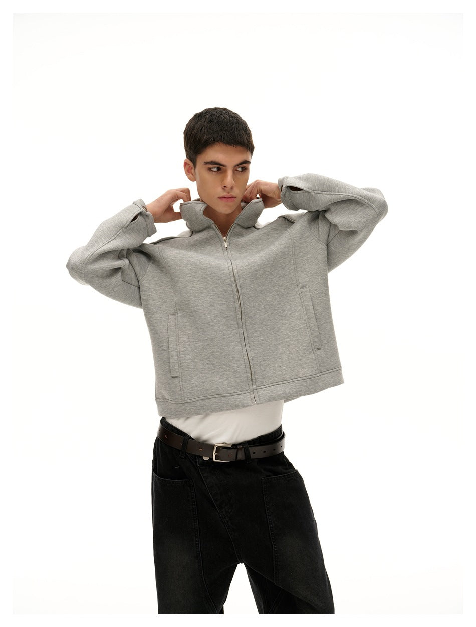 Model adjusting the raised collar of a light gray zip-front jacket with black pants.