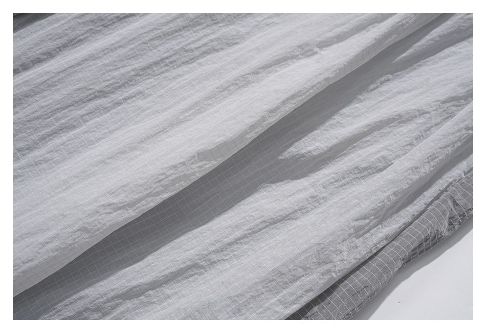 Close-up of light gray fabric with a fine white grid, arranged in soft folds.