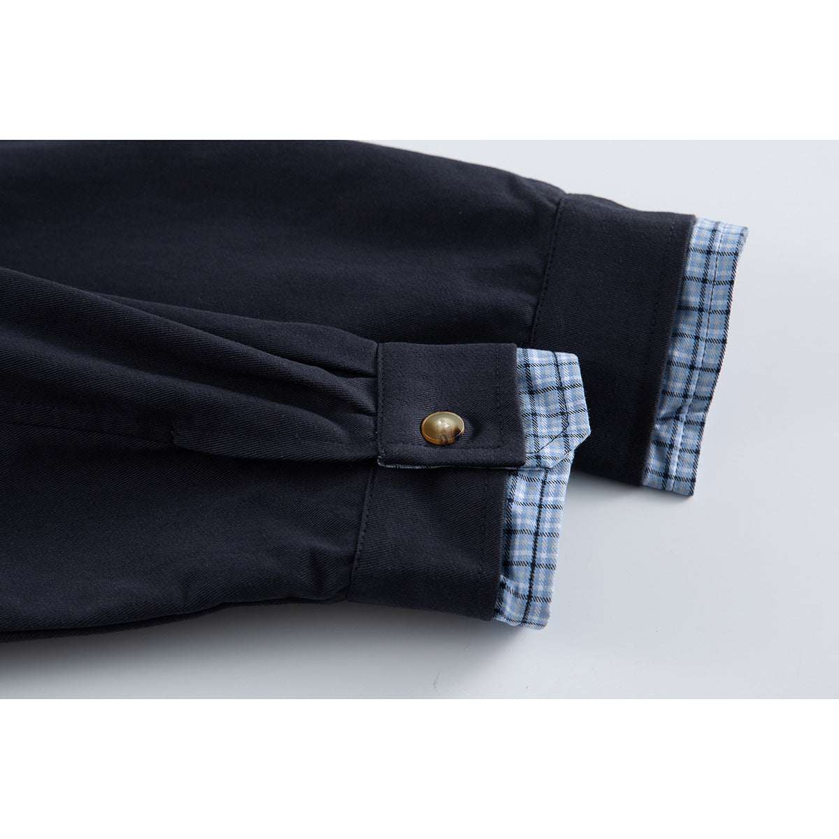 Close-up of a dark navy jacket cuff with a button tab and light blue plaid lining.