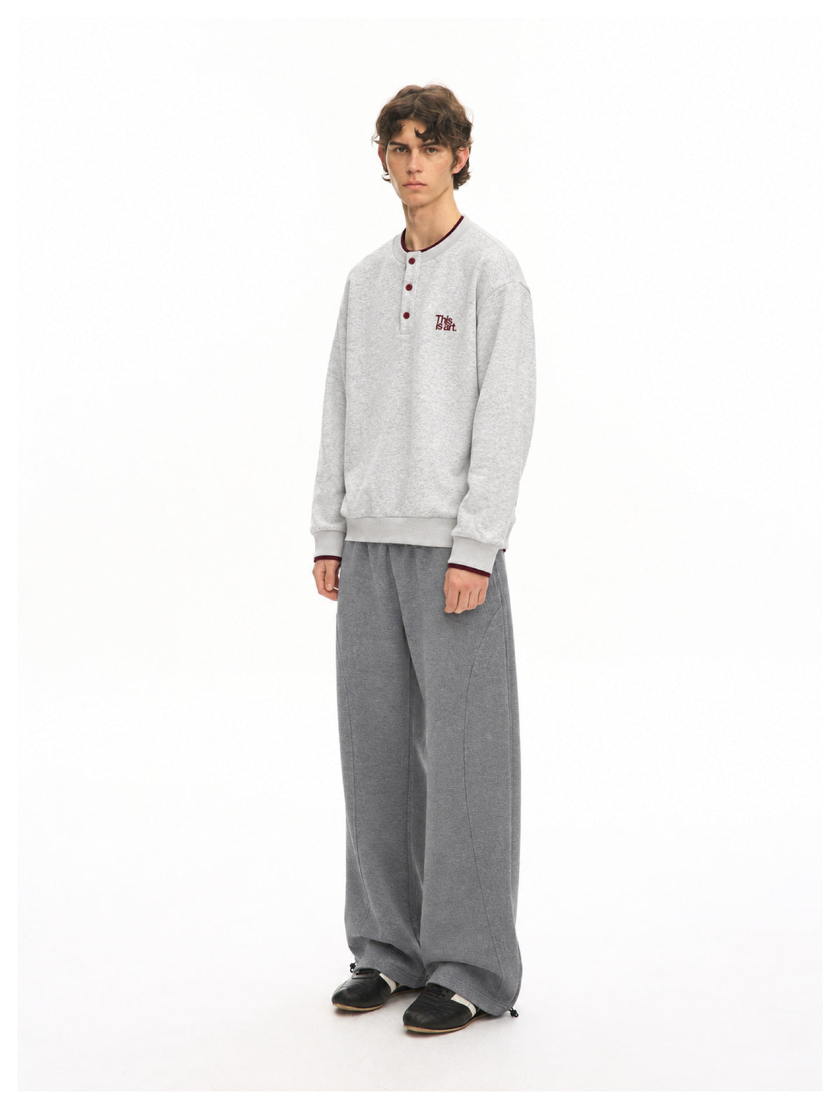 Three-quarter front view of a model wearing a light gray button-neck sweatshirt and wide-leg dark gray pants.