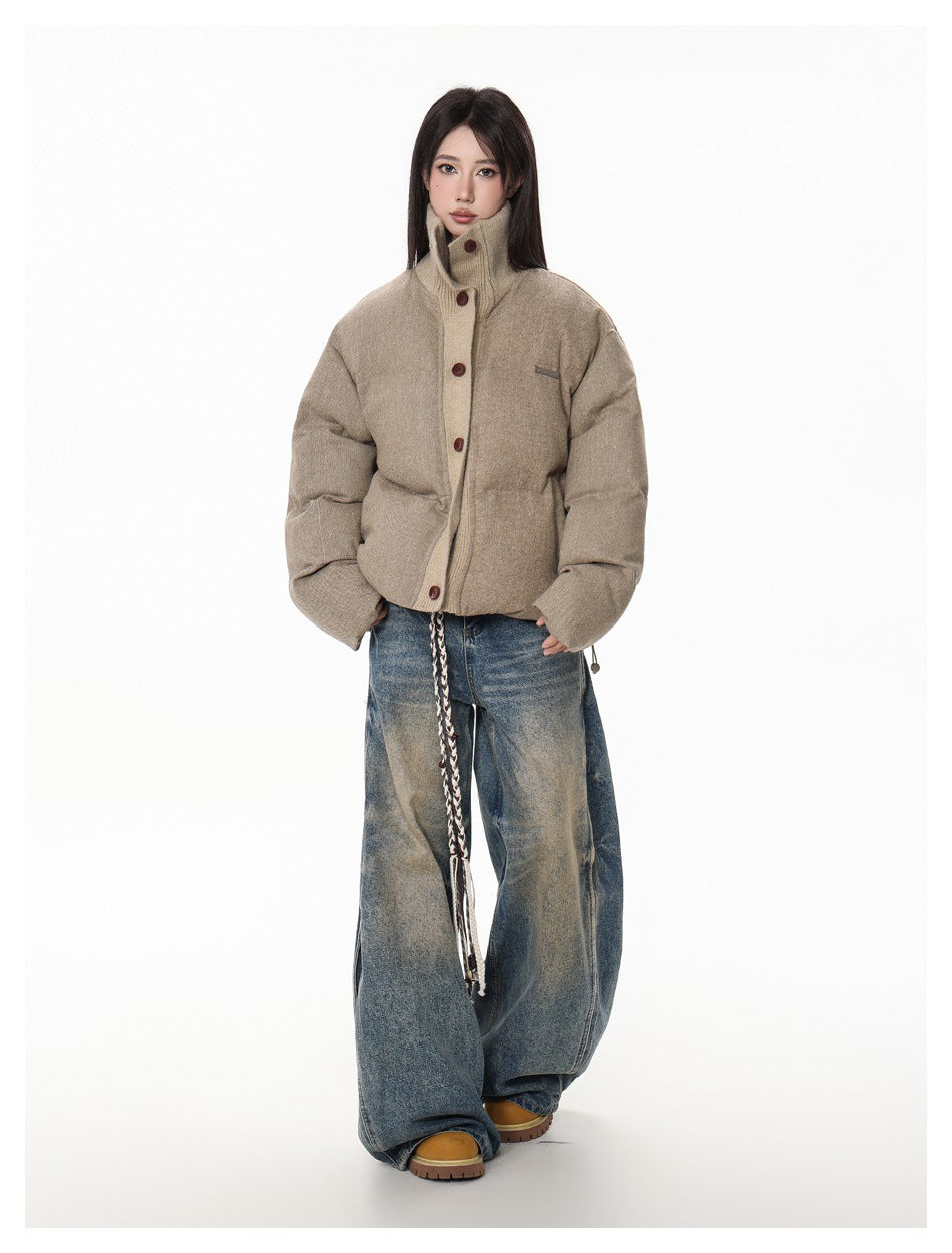 Model wearing a taupe padded jacket with a high buttoned collar and oversized sleeves, paired with wide-leg blue jeans.