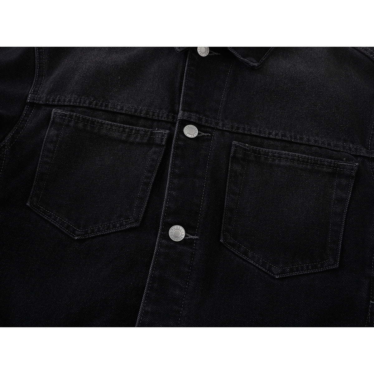 Close-up of a black denim jacket front showing two flapless chest pockets and silver buttons.