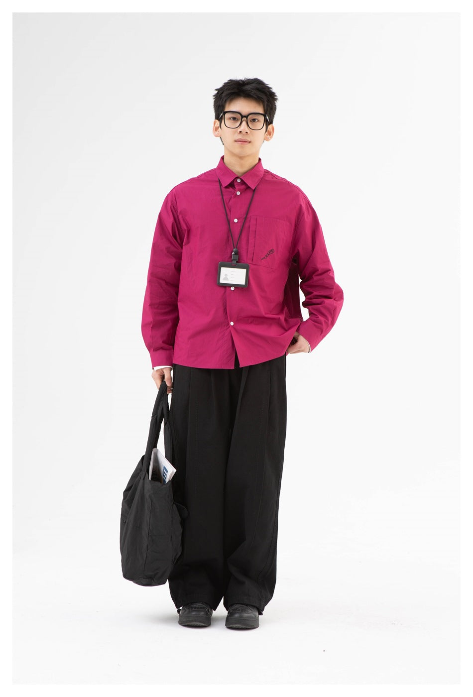 Full-length front view of a model in a magenta button-up shirt and wide black trousers, carrying a black tote bag.