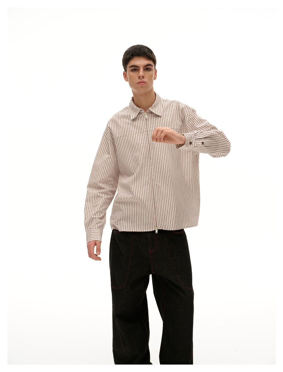 Model wearing a cream shirt with fine brown vertical stripes, pointed collar, front zipper and long sleeves.