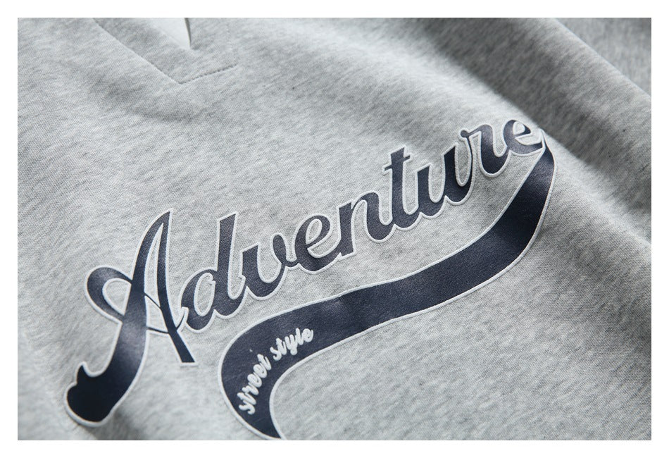 Close-up of the navy script “Adventure” graphic with a small white text accent on gray sweatshirt fabric.