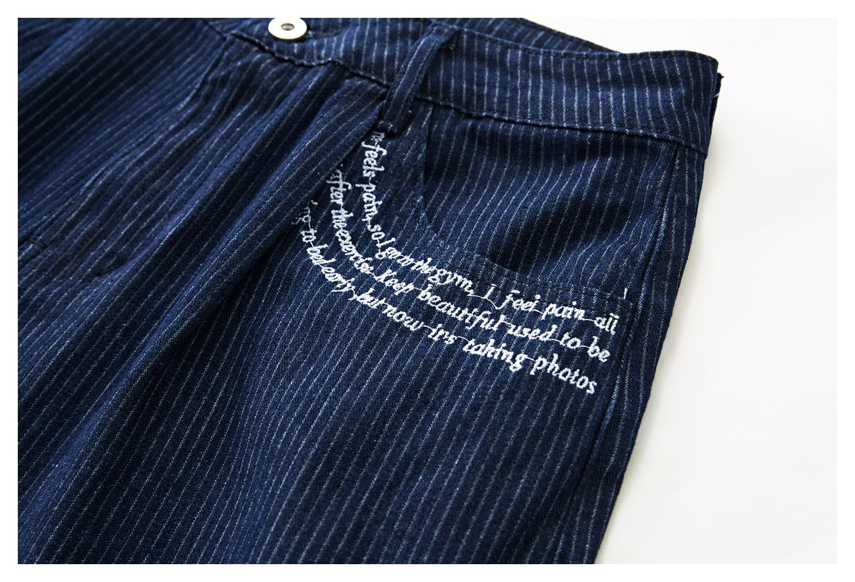 Close-up of a front pocket on navy pinstriped shorts with white script embroidery and a visible waistband button.