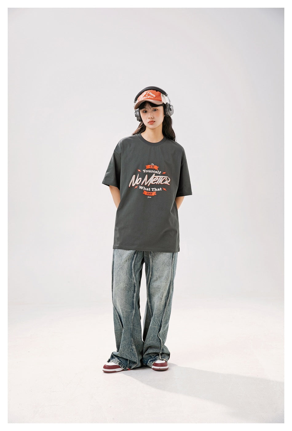 Model wearing a charcoal gray oversized graphic T-shirt with loose faded jeans, front view.