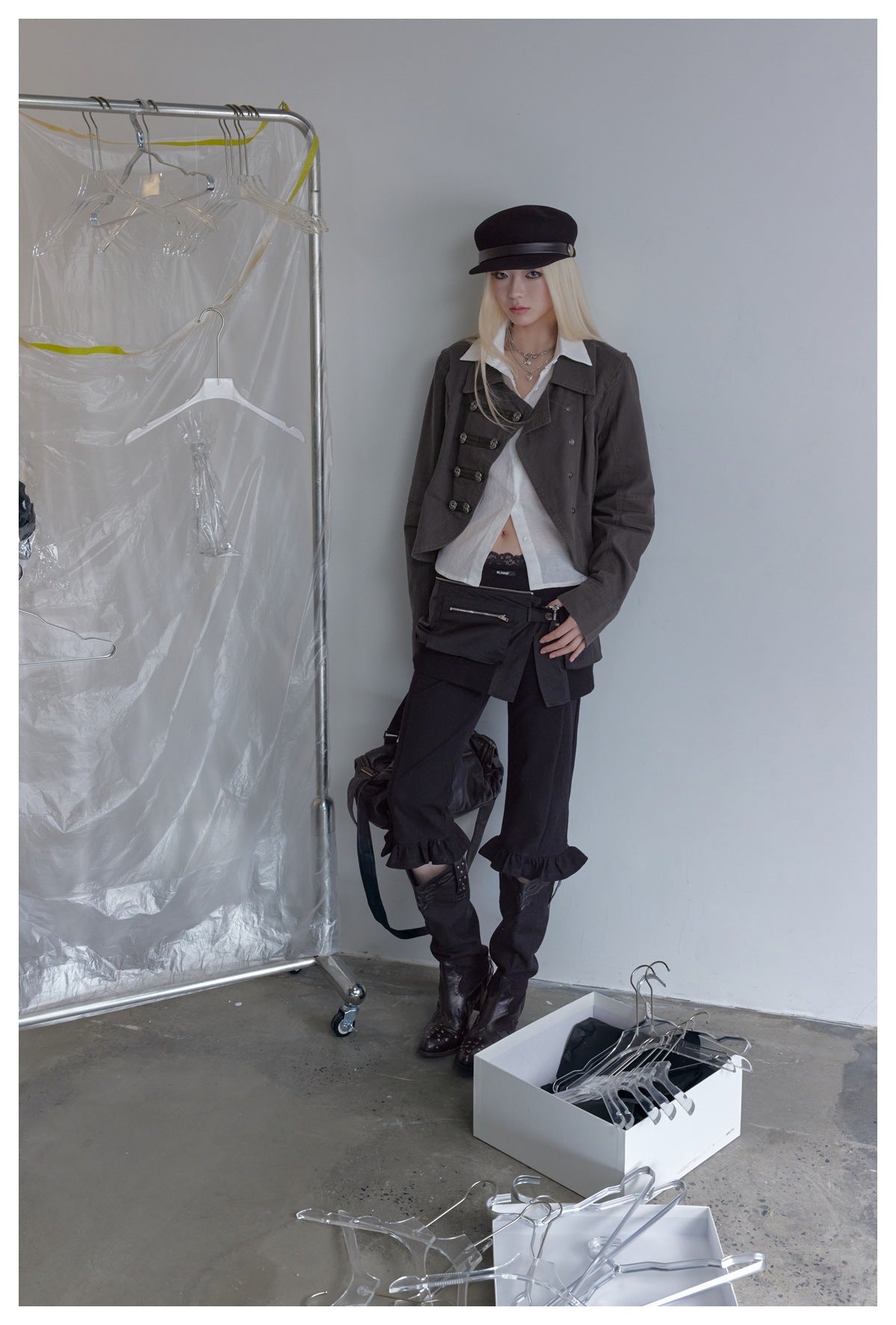 Model wearing a dark gray cropped jacket over a white shirt with black cap, dark ruffle-hem pants and boots