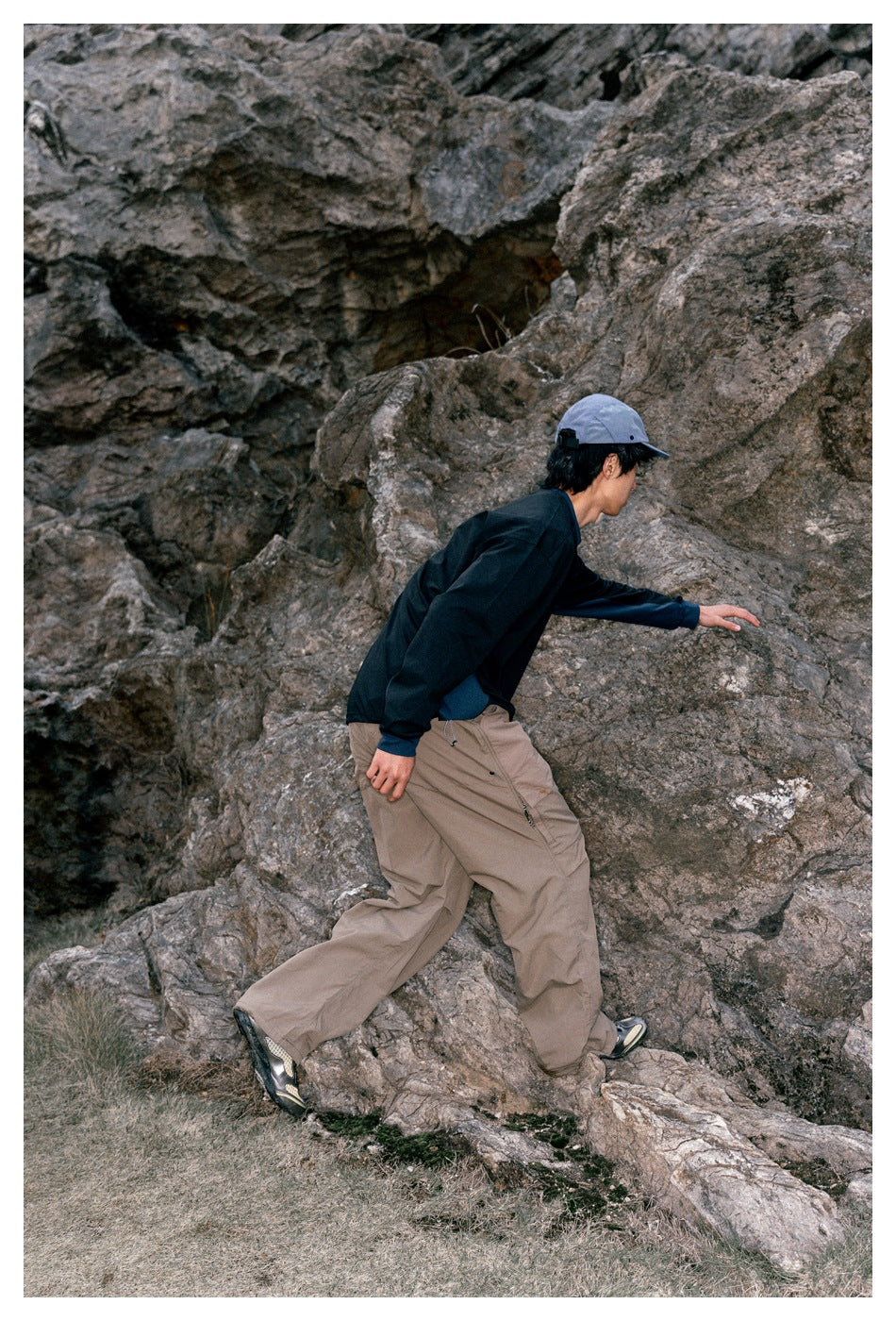 Side and back view of a model in a dark long-sleeve shirt and loose taupe cargo pants climbing over rocks.