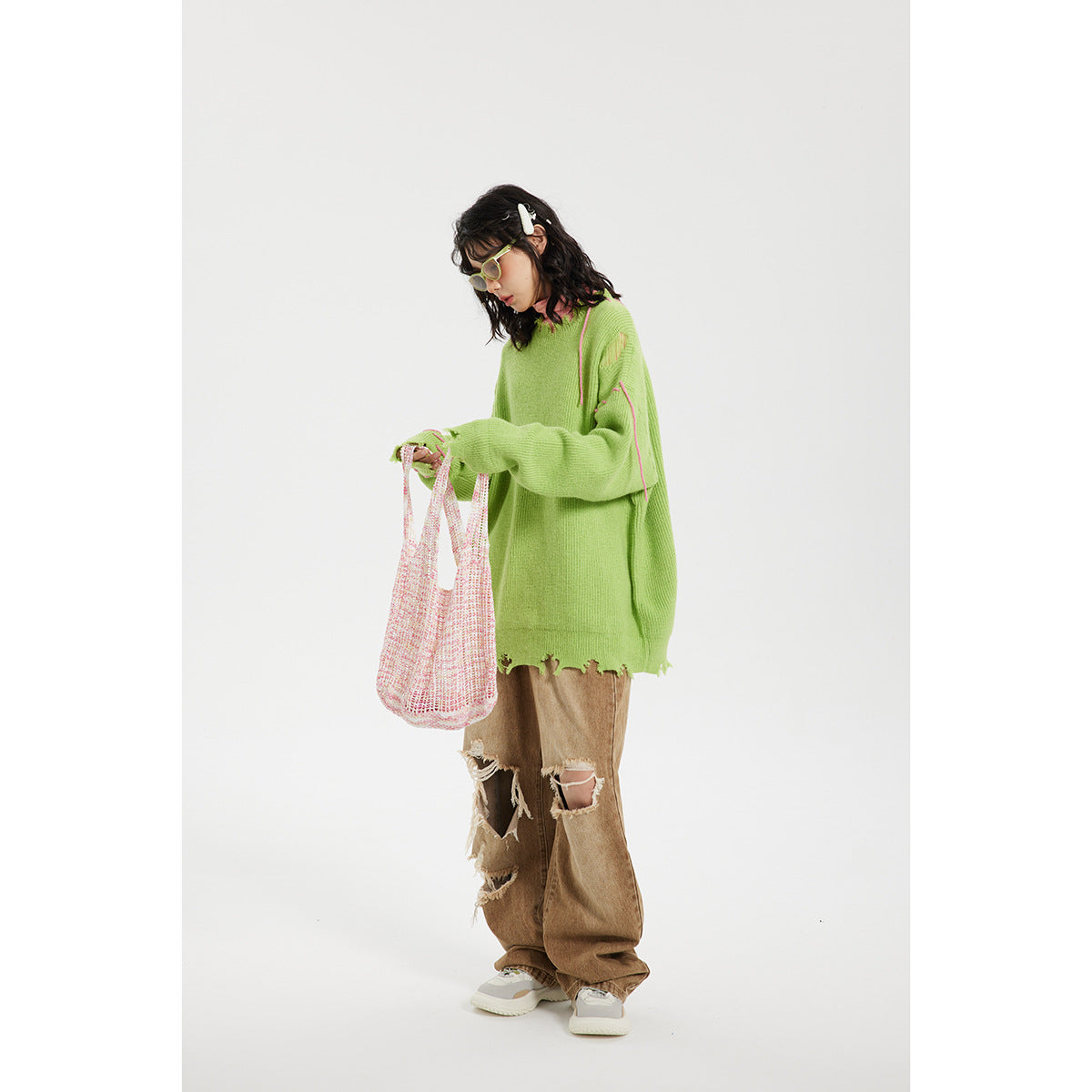 Model wearing an oversized lime-green sweater with pink stitched accents and a distressed hem, shown from the front.