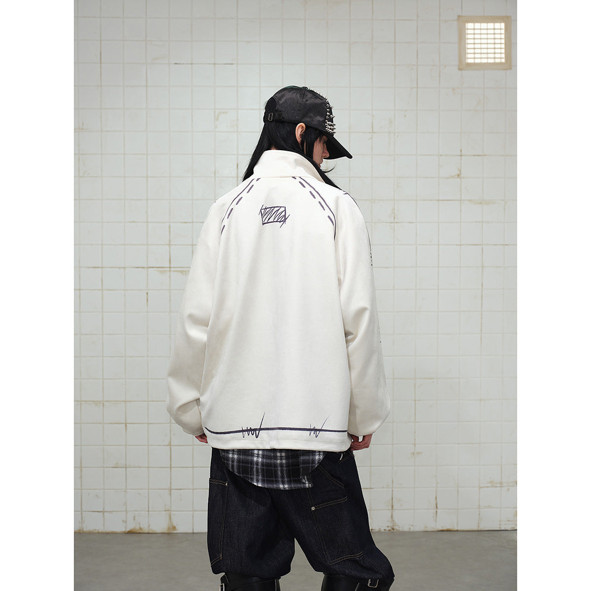Rear view of a model wearing a cream jacket with black sketch graphics and dark jeans.