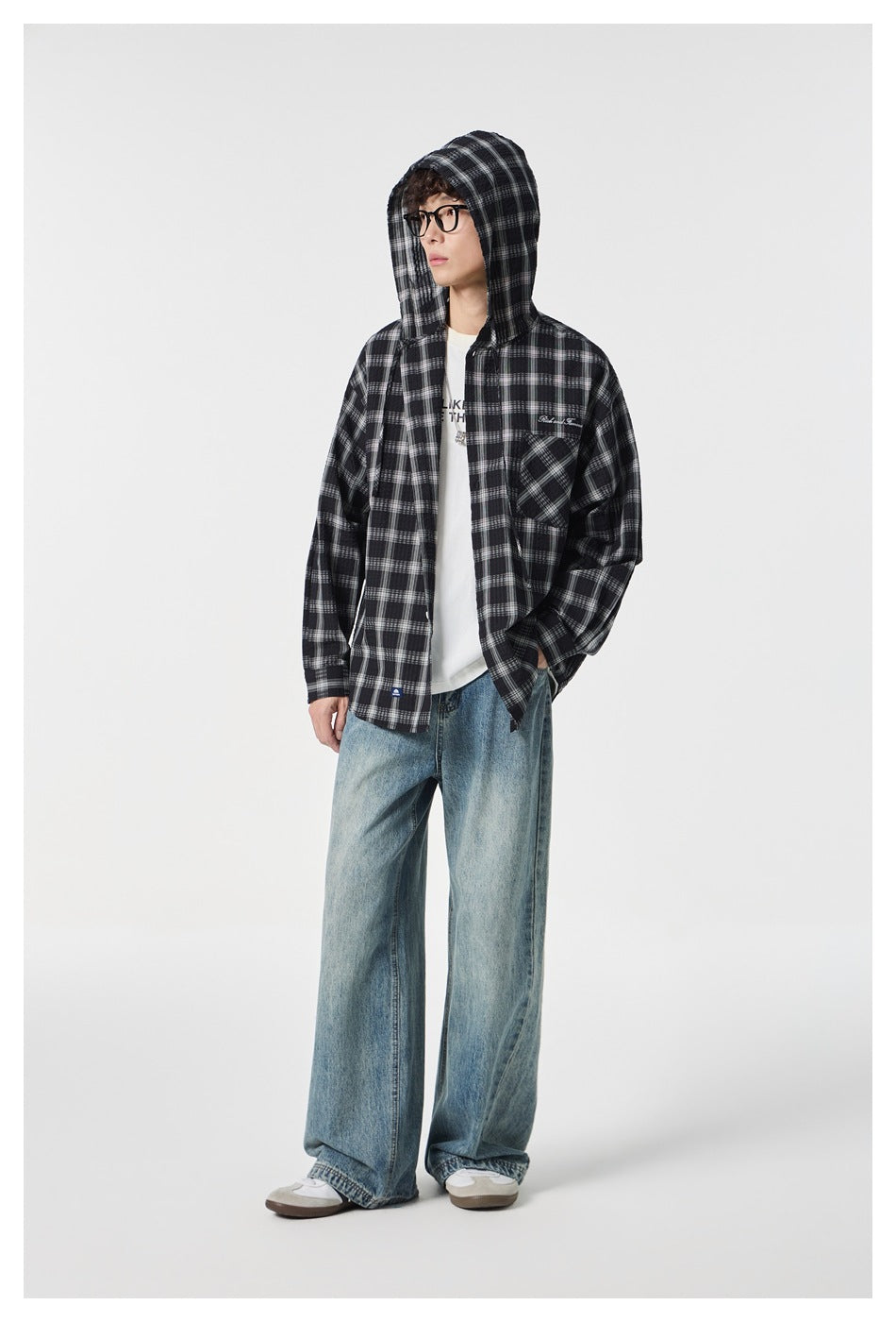 Full-length model wearing a black-and-white plaid hooded button-up shirt with the hood up and loose blue jeans.