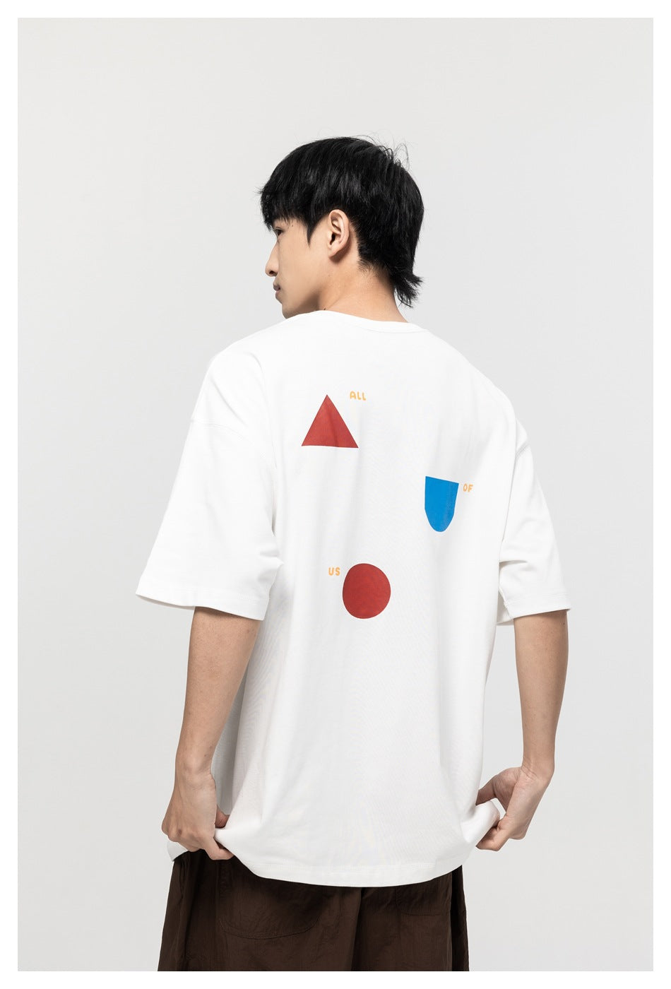 Back view of a model wearing a white T-shirt with red and blue geometric graphics and small words.