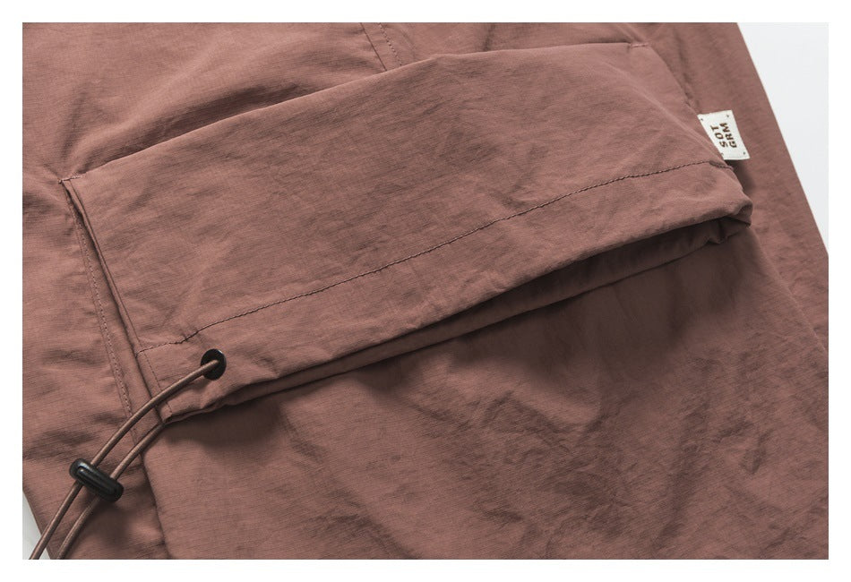 Close-up of a muted mauve-brown garment with a stitched flap and black drawcord toggle.