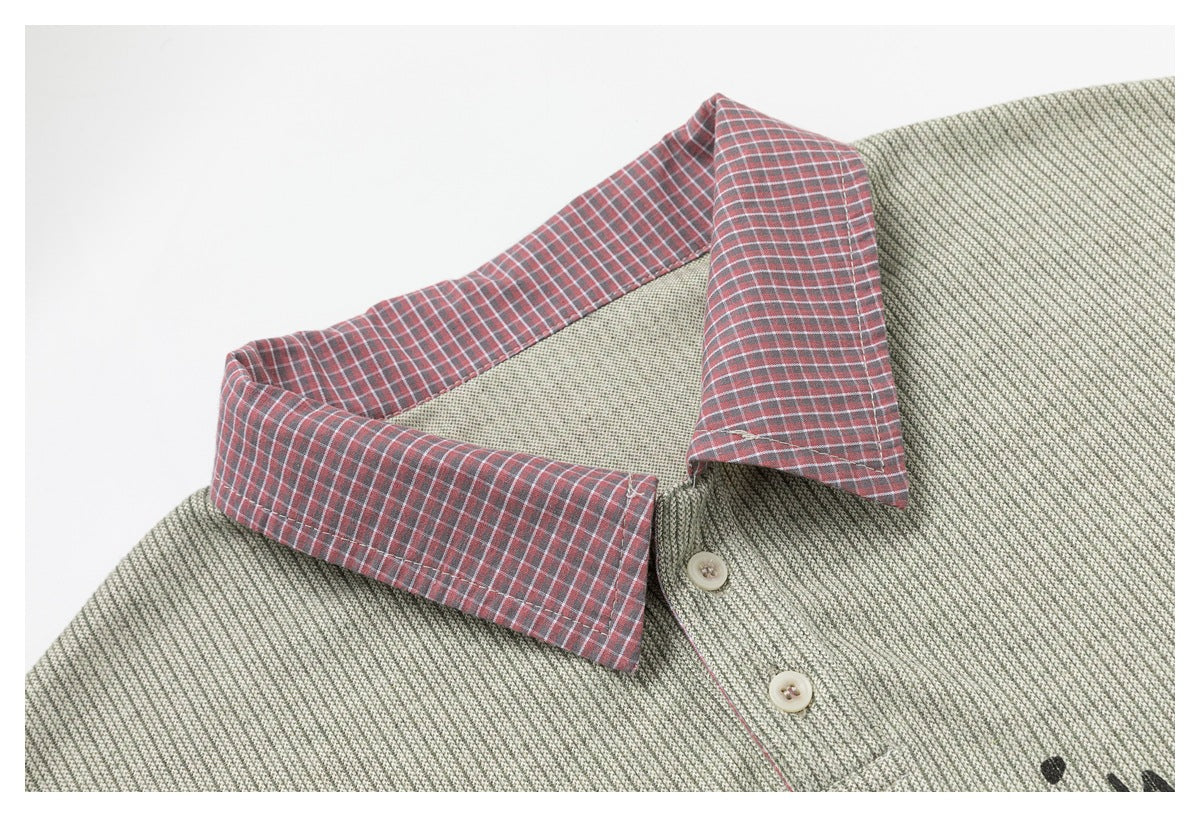 Close-up of a sage-gray textured shirt with a red plaid collar, cream buttons, and a partial black print.