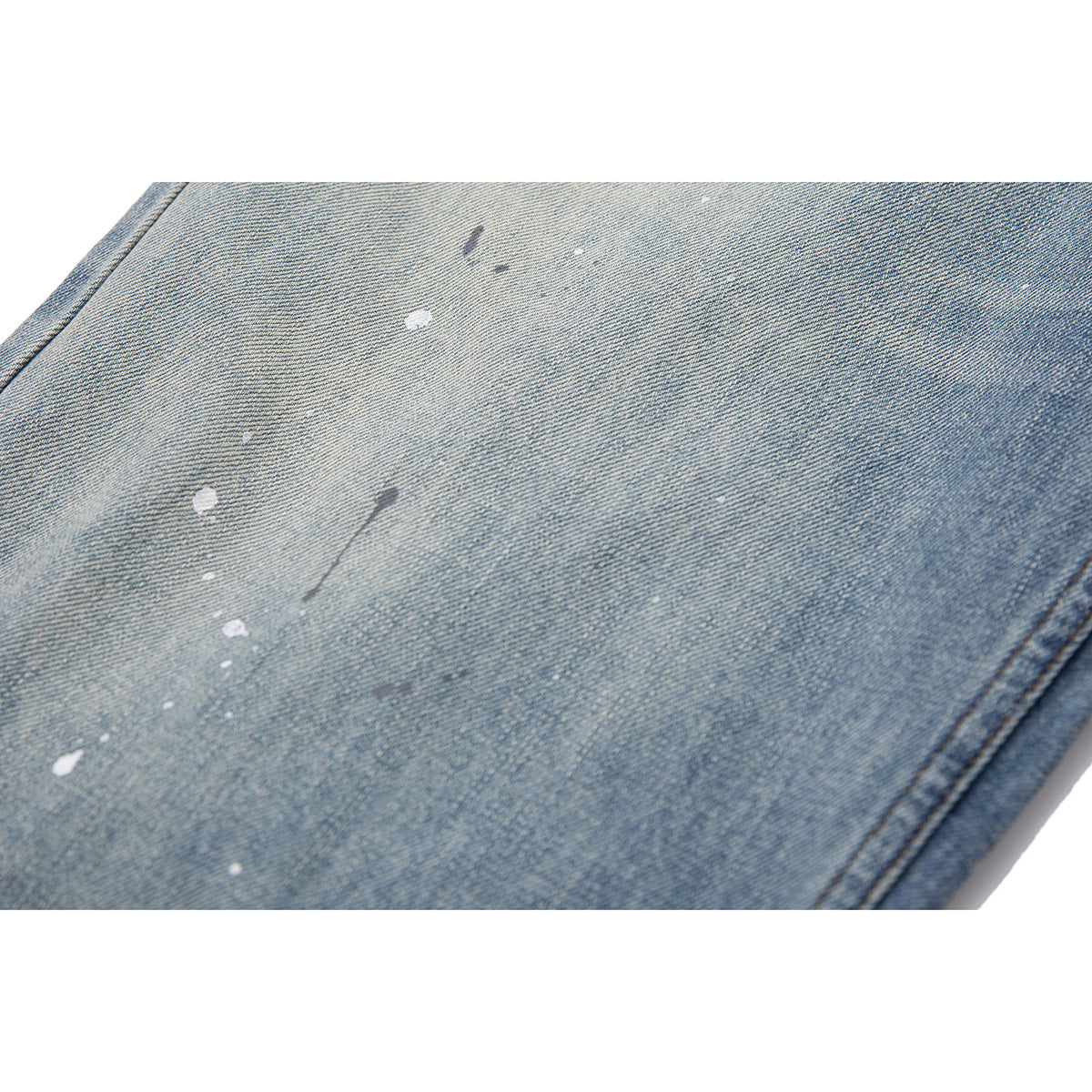 Close-up of light blue washed denim with scattered white and dark paint-like marks.