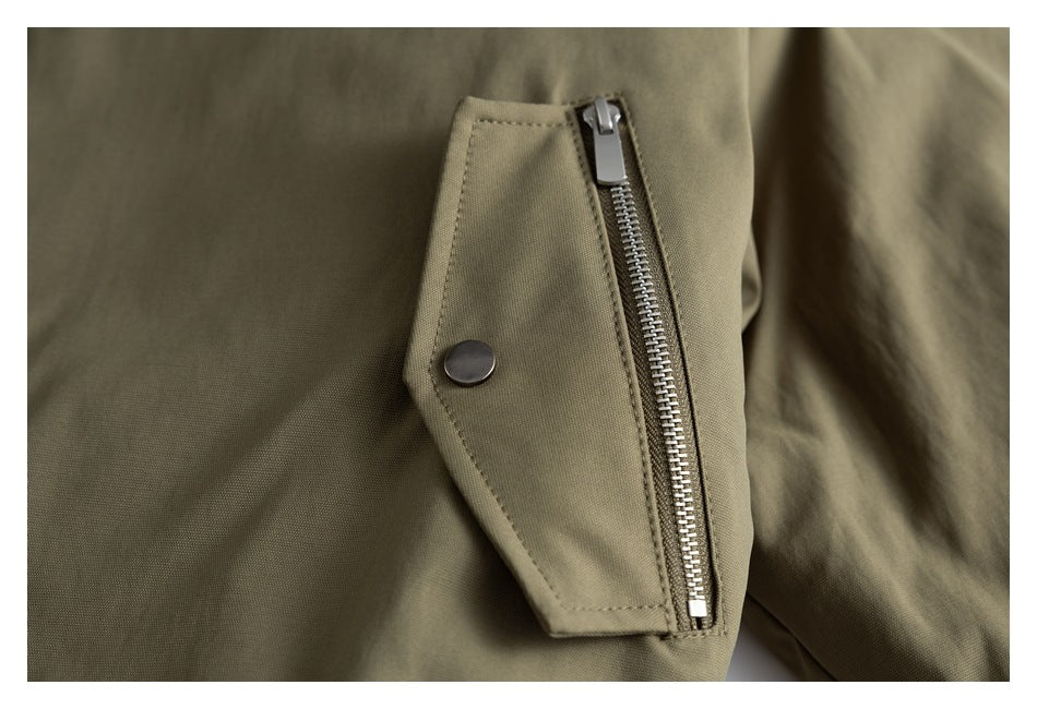 Close-up of an olive jacket sleeve zipper pocket with a metal zipper and snap tab.