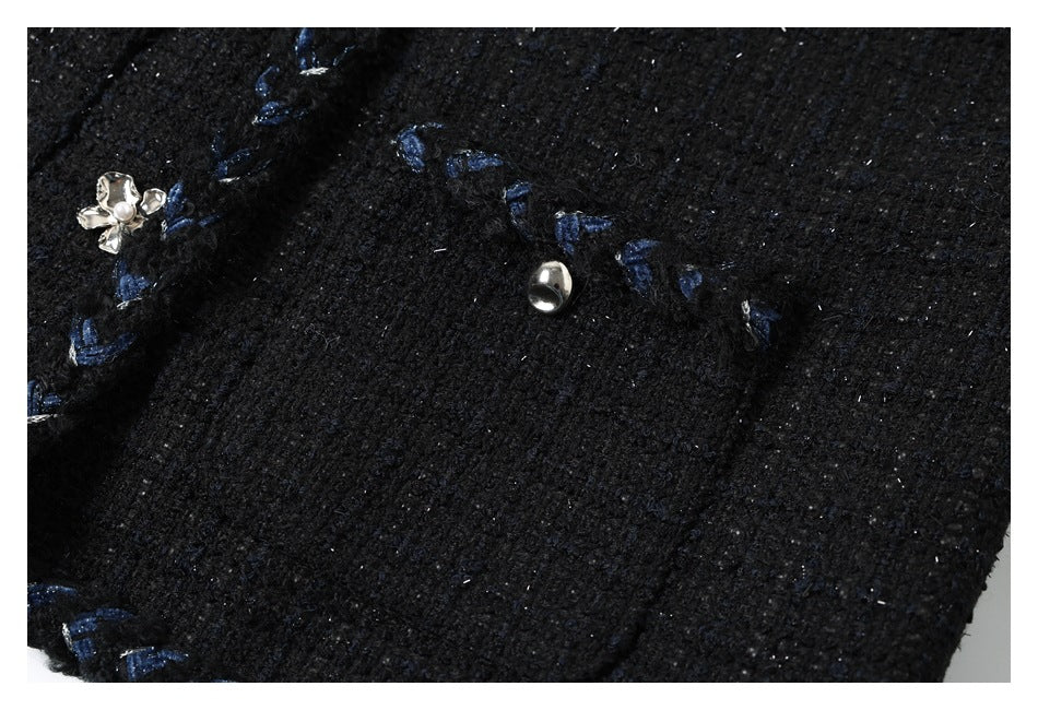 Close-up of black textured fabric with blue stitching and small silver decorative buttons.