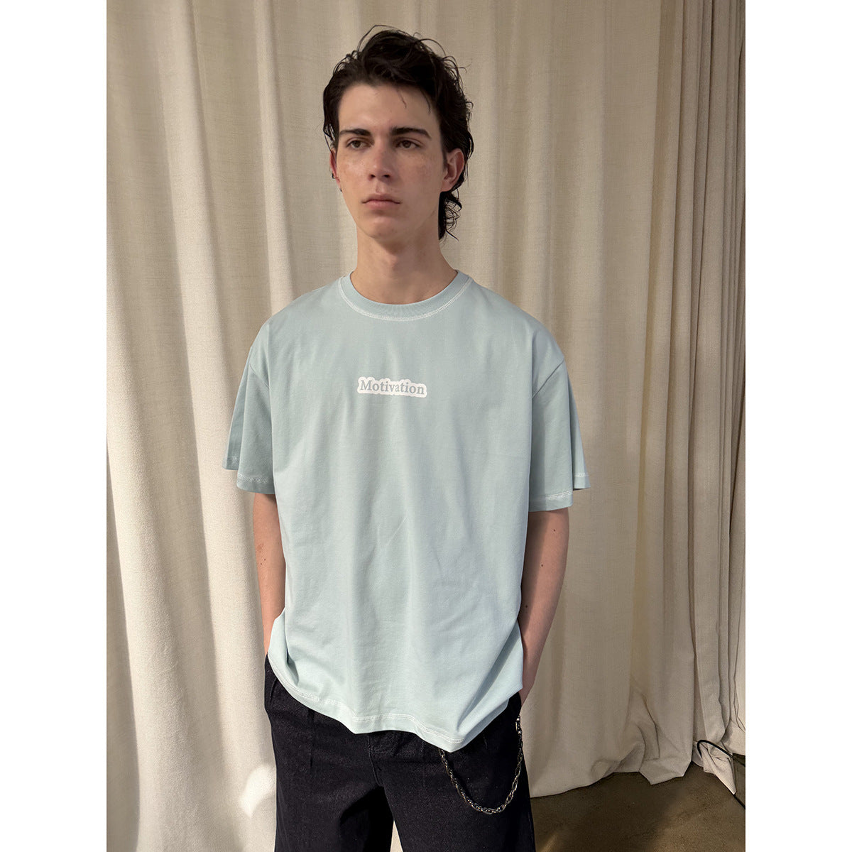 Model wearing a pale blue oversized T-shirt with a small white chest graphic and black jeans.