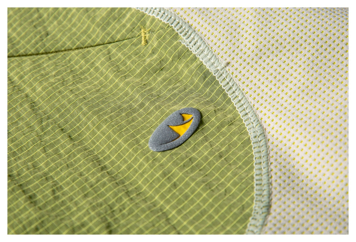 Close-up of a gray-and-yellow emblem on an olive-green panel, bordered by cream dotted fabric.