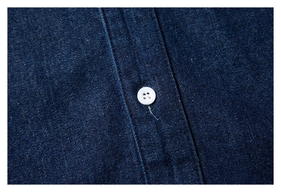 Close-up of a white button and stitching on the dark indigo shirt fabric.