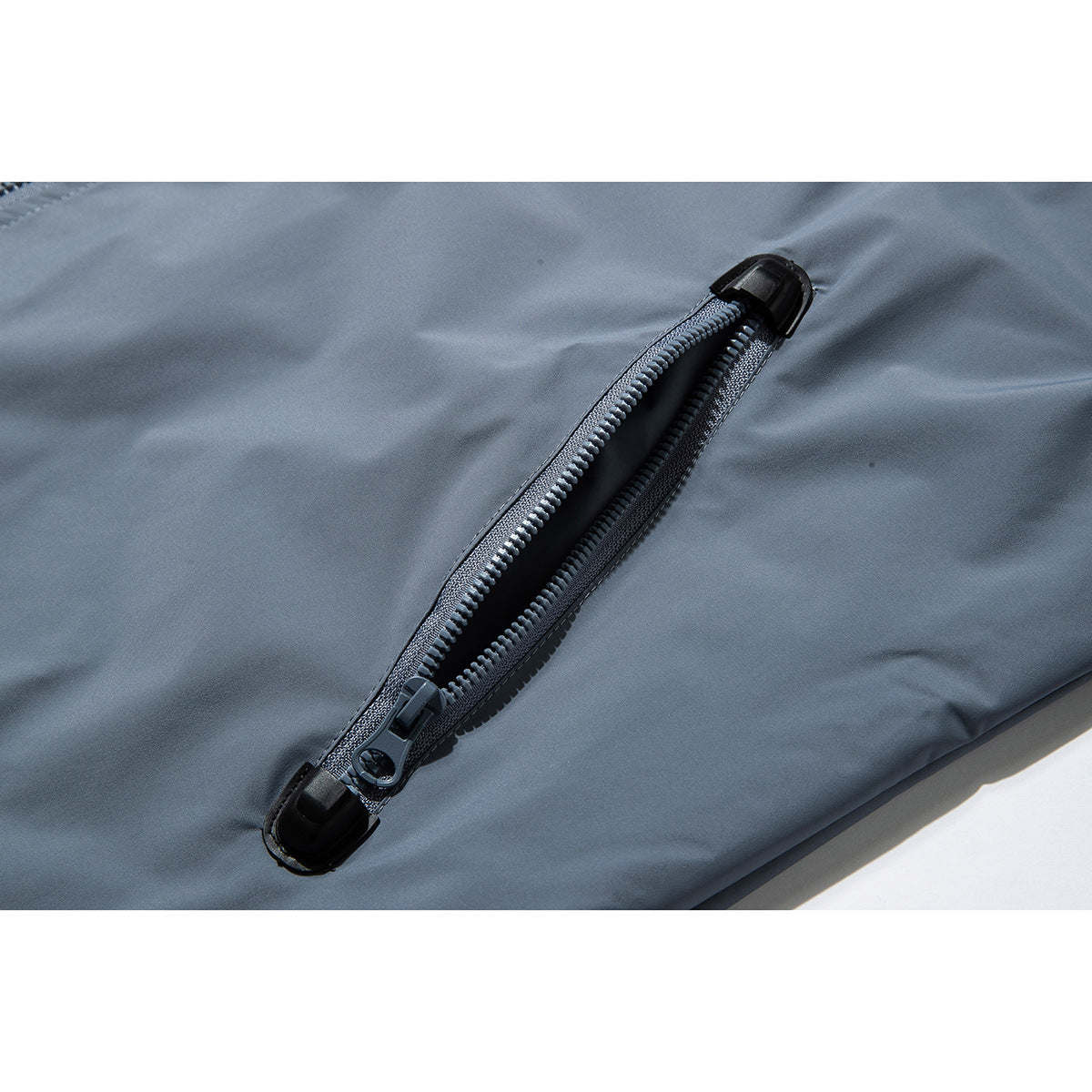 Close-up of an open black zipper with reinforced ends on slate-blue jacket fabric.