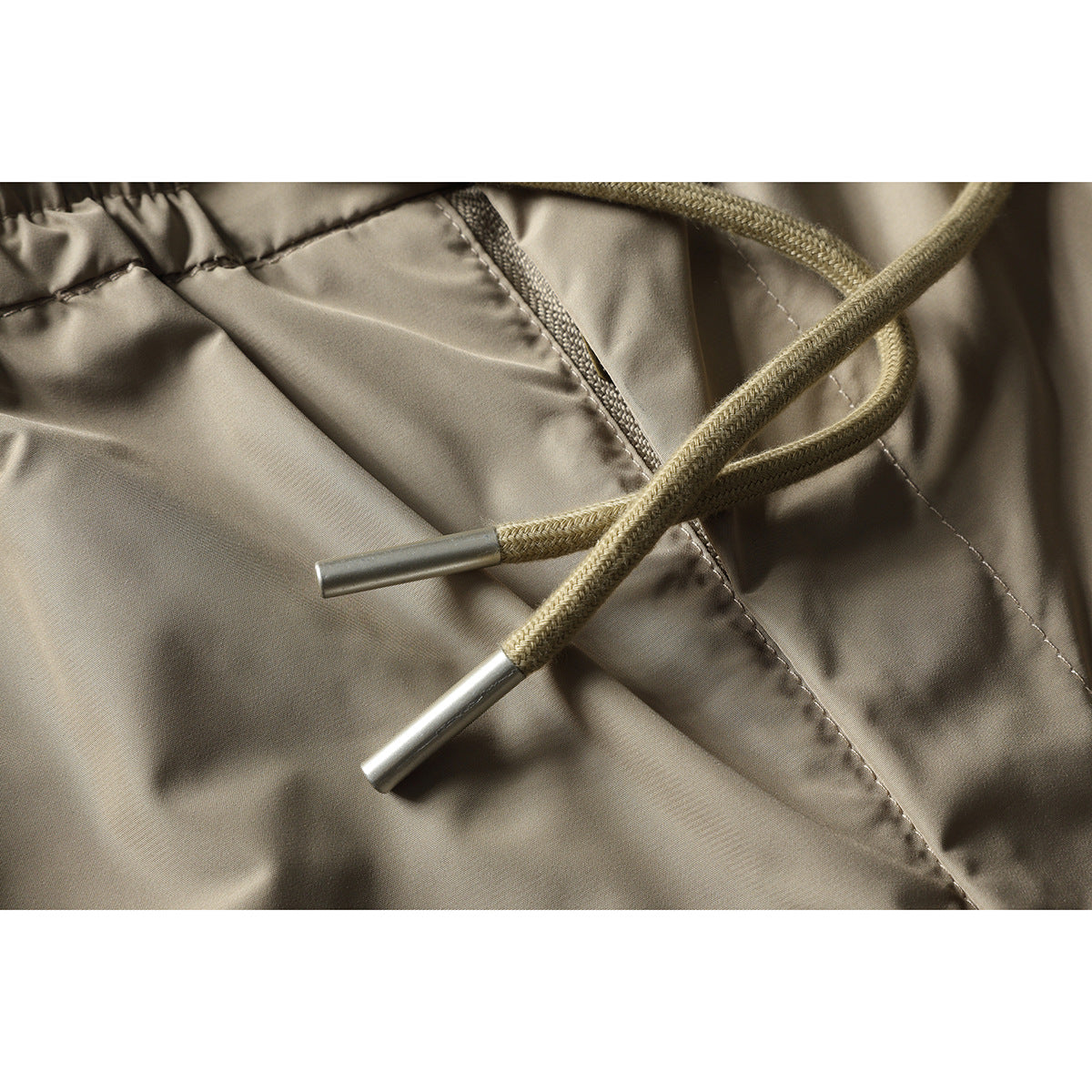 Close-up of beige trouser drawstrings with metal tips against the front fabric and seam.
