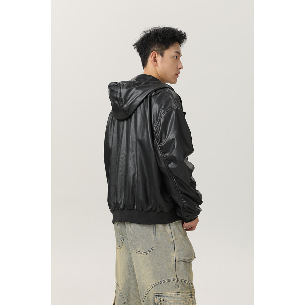 Side and back view of a model wearing a black hooded jacket with a ribbed hem and loose faded cargo jeans.