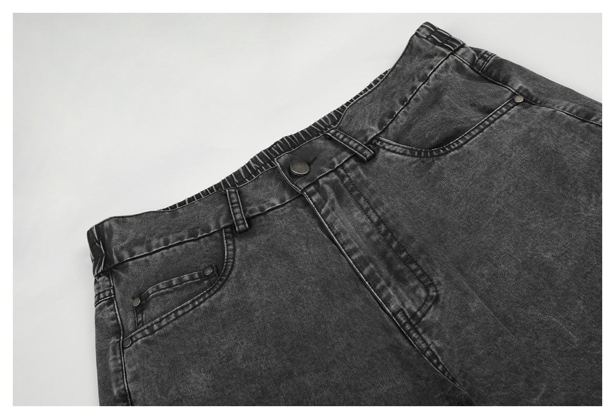 Angled close-up of the charcoal-gray jeans' front waistband, button, fly, belt loops, and pockets.