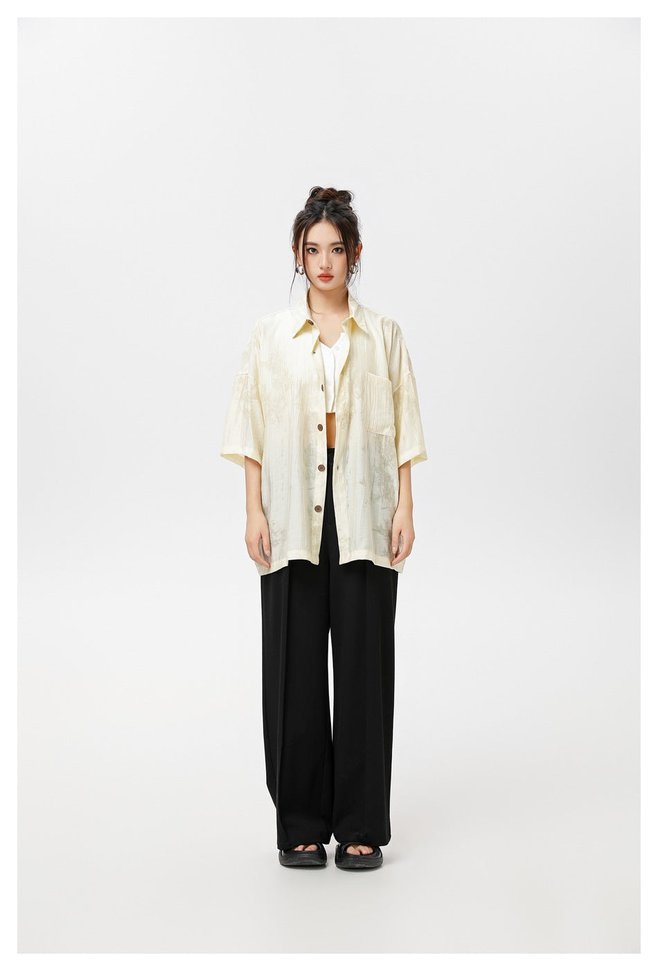 Model wearing an oversized pale yellow short-sleeve button shirt open over a white top with black wide-leg trousers