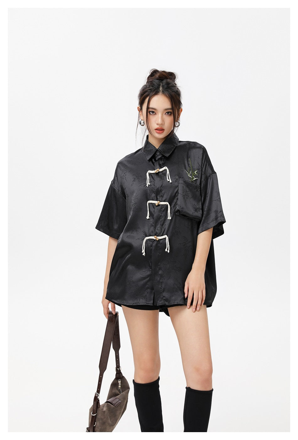 Closer view of a model wearing a black patterned short-sleeve shirt with rope frog closures and bamboo embroidery on the