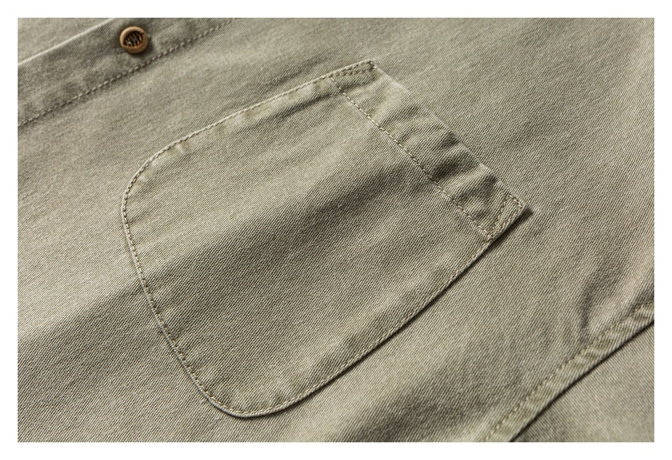 Close-up of a khaki-olive garment with a large stitched pocket, tan button, and visible twill texture.