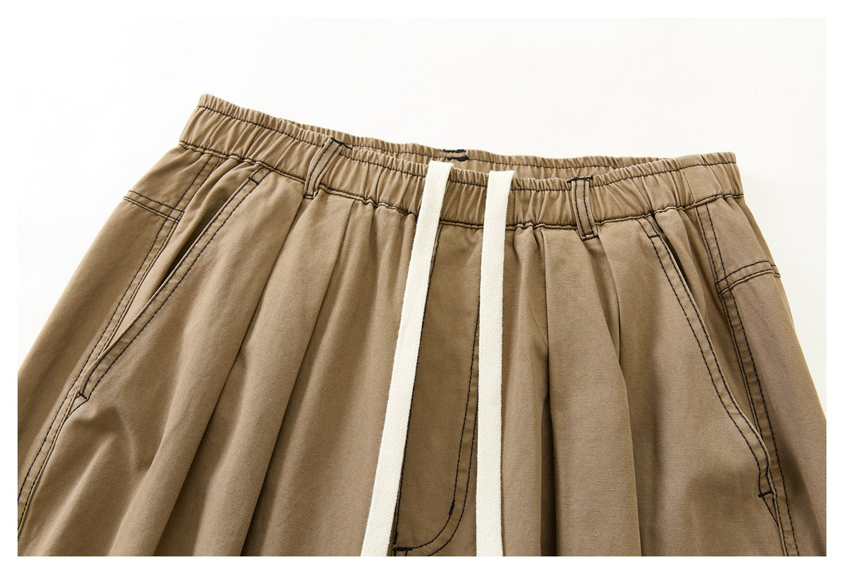 Close-up of tan wide-leg pants showing an elastic waistband, white drawstrings, pleats, and angled front pockets.