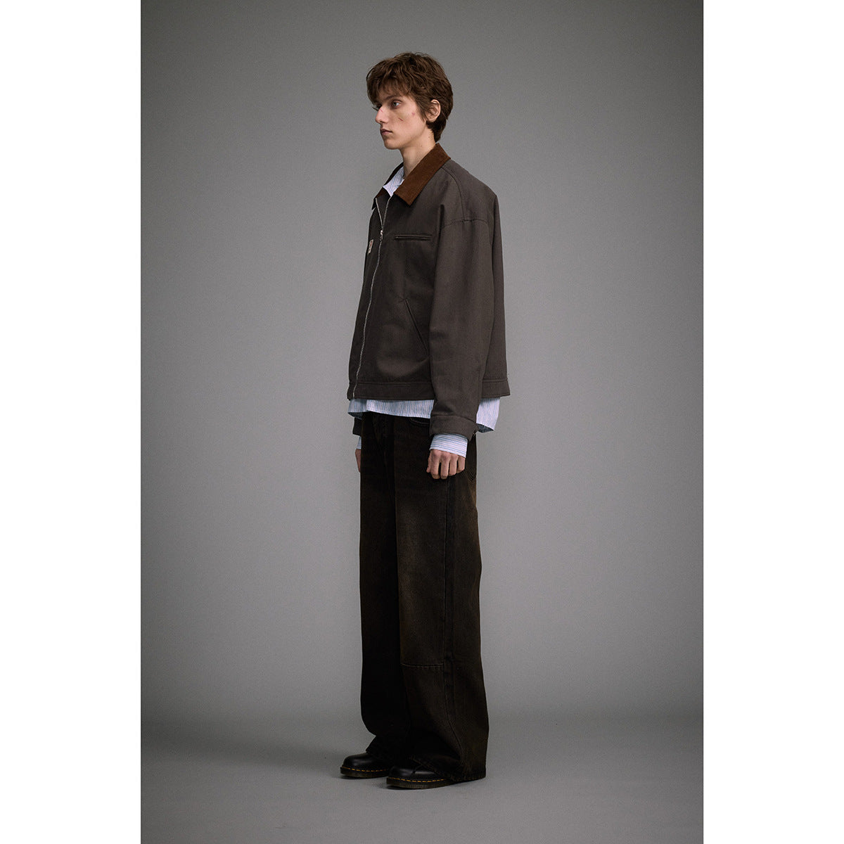 Model in profile wearing a dark brown zip-front jacket with a brown collar and chest pocket.
