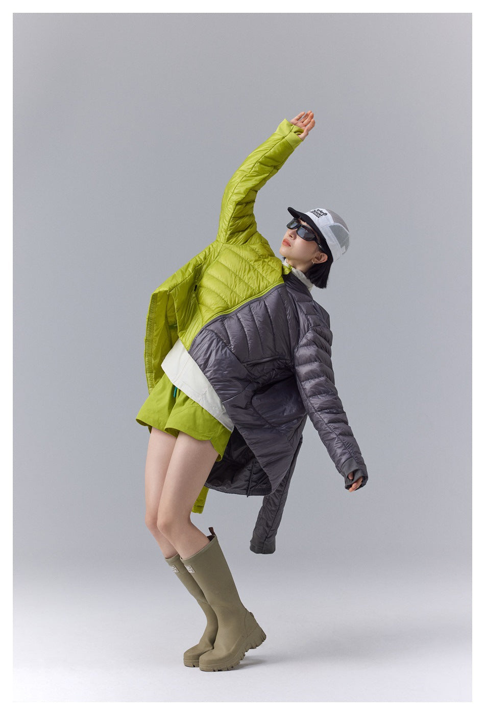 Model in a two-tone lime and charcoal quilted jacket, posed with one arm raised.