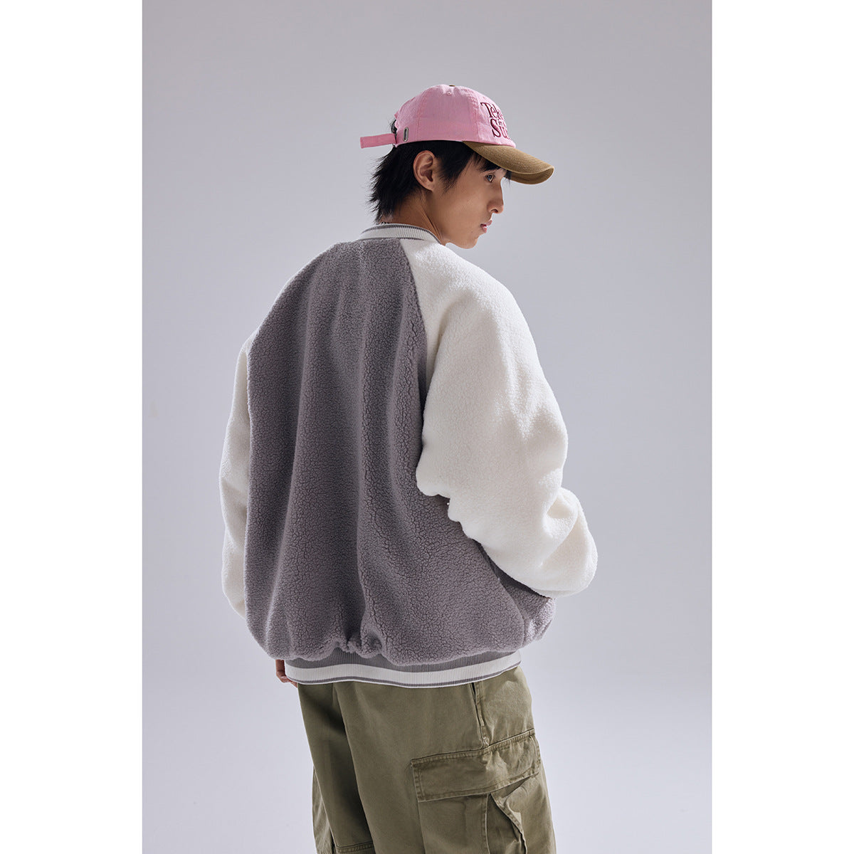 Model shown from behind in a gray-and-white color-block fleece varsity jacket with striped ribbed hem and cuffs.