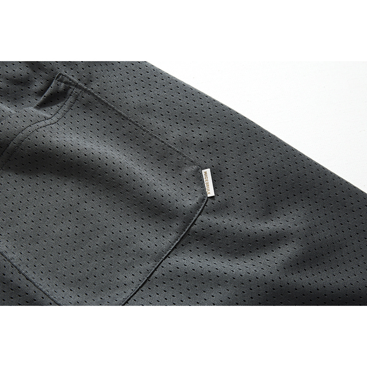Close-up of charcoal perforated mesh shorts showing a stitched pocket and small fabric tag.