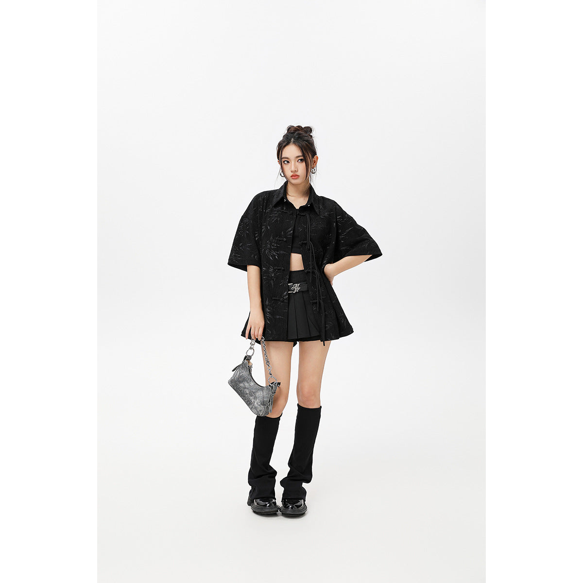 Model wearing a black short-sleeve patterned shirt with tie closures, a black crop top and pleated skirt.