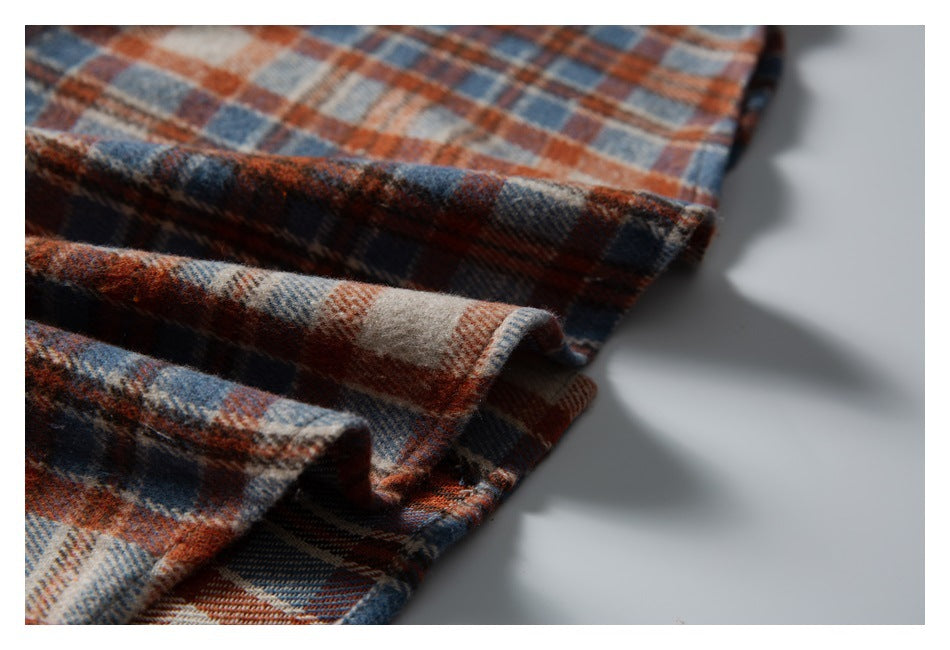 Close-up of the folded edge of a rust, navy and cream plaid garment on a light background.