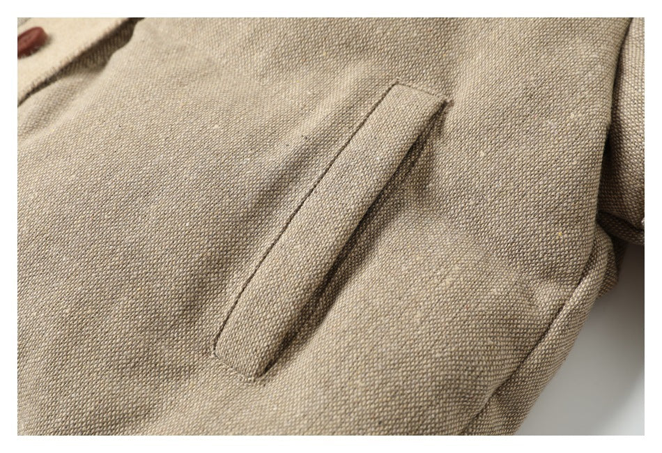 Close-up of a beige woven jacket showing a slanted welt pocket and a partial brown button.