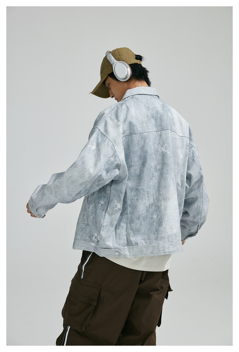 Closer rear view of a model wearing a light gray mottled jacket with a wide back yoke and buttoned hem tabs.